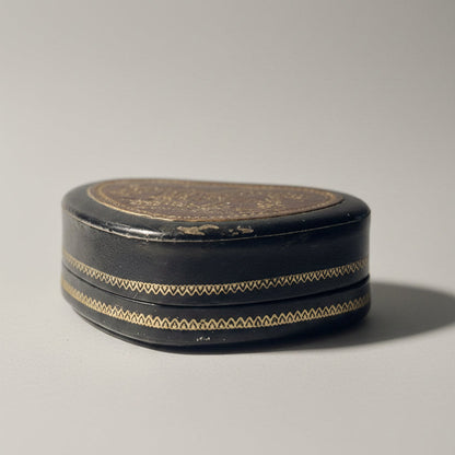 Round black decorative box with gold patterns on a white surface