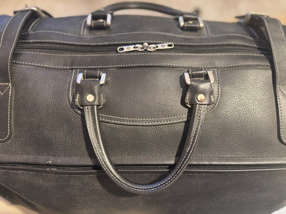 Black leather duffel bag with silver zippers on a neutral background