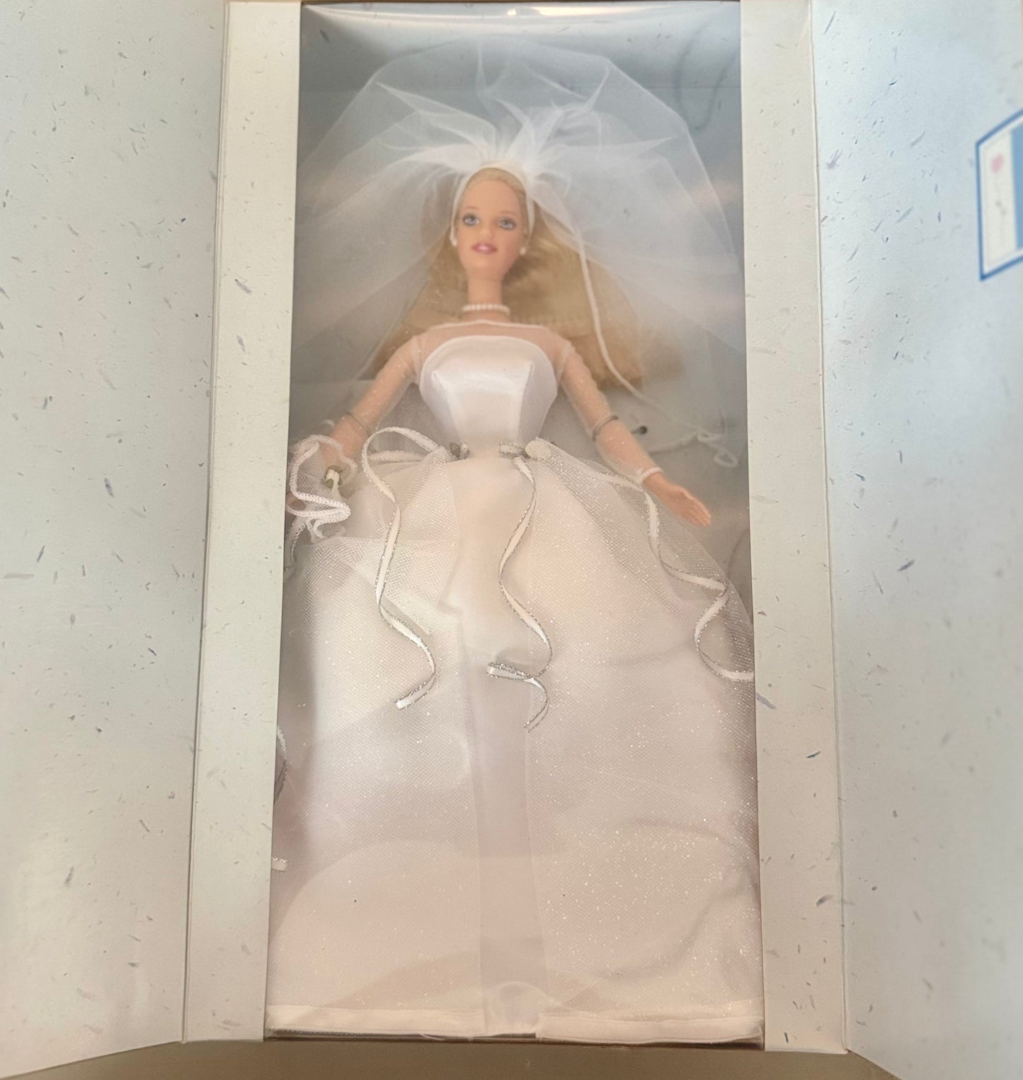 A blonde fashion doll dressed in a white wedding gown and veil, displayed inside an open white box.