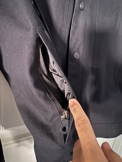 Close-up of a dark gray jacket with a zipper being pointed to by a hand.