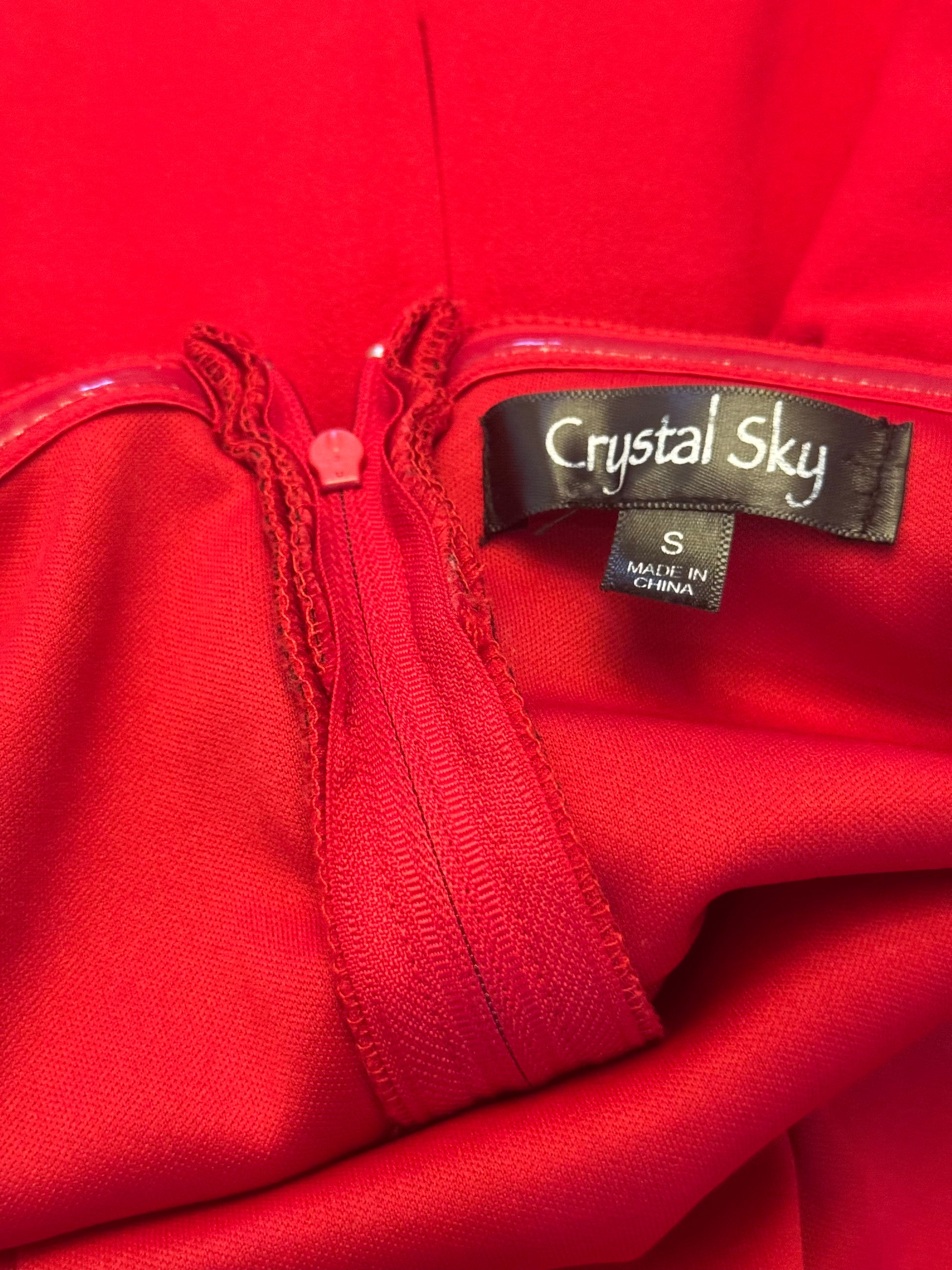 Close-up of a bright red garment with a black brand label reading Crystal Sky and a size tag reading S Made in China.