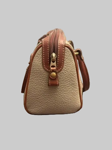 A small pebbled leather handbag in beige and brown, shown from the back on a dark wood floor in front of a window with blinds.