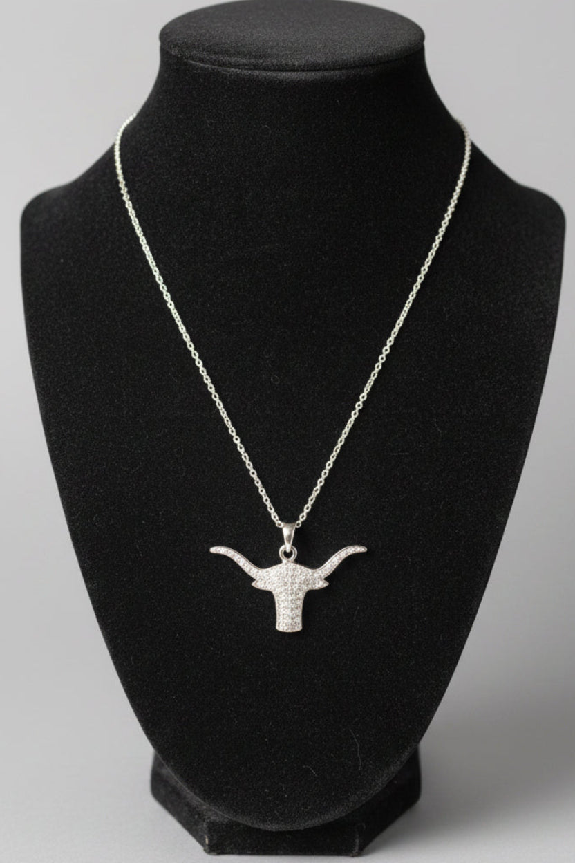 A silver-toned chain necklace with a longhorn-shaped pendant displayed on a black velvet jewelry bust, set against a blurred indoor background.