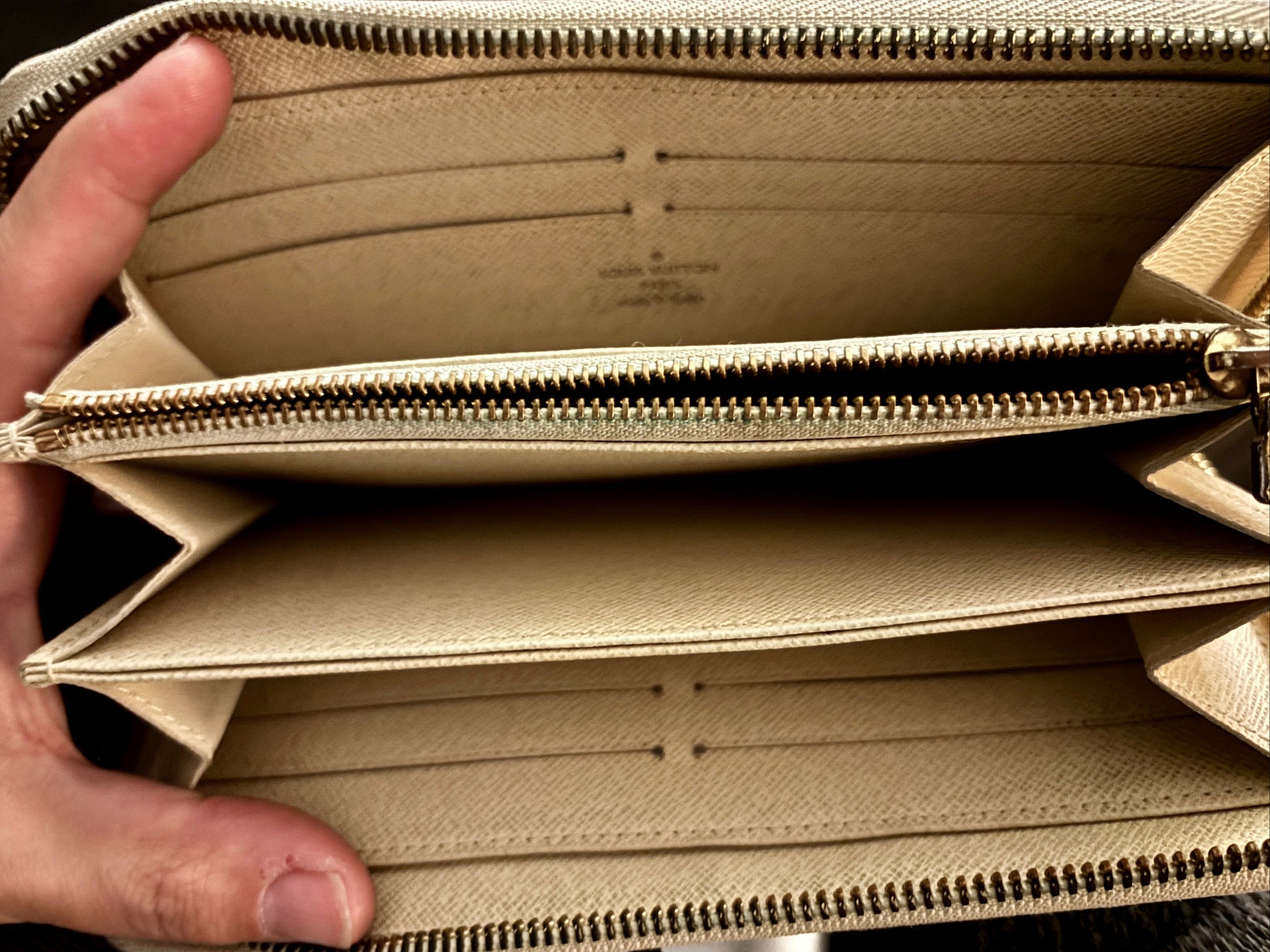 Beige wallet with a hand holding it open, showing the interior.