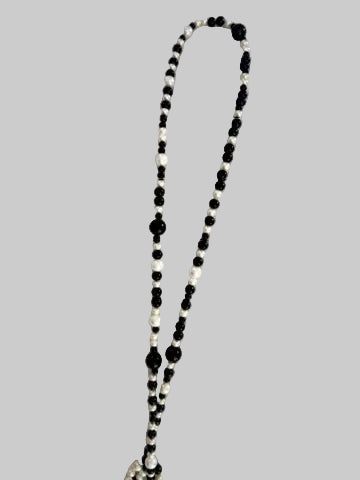 A long beaded necklace with alternating black and white beads, laid out on a soft white fabric background.