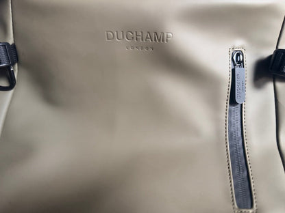 Close-up of a beige DUCHAMP London waterproof backpack with a vertical zipper pocket and black straps.
