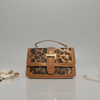 Leopard print handbag with brown leather accents on a light gray surface