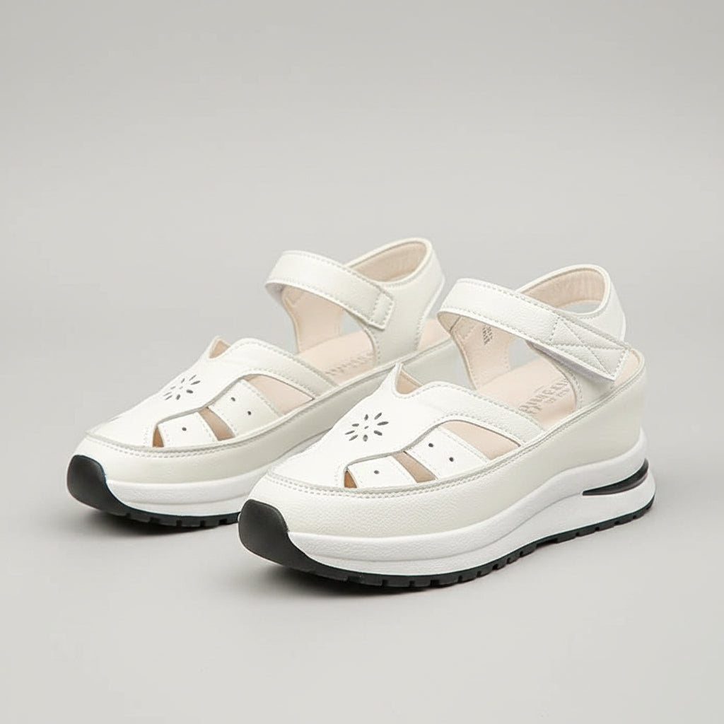 White sandals worn with light gray pants on a stone surface.