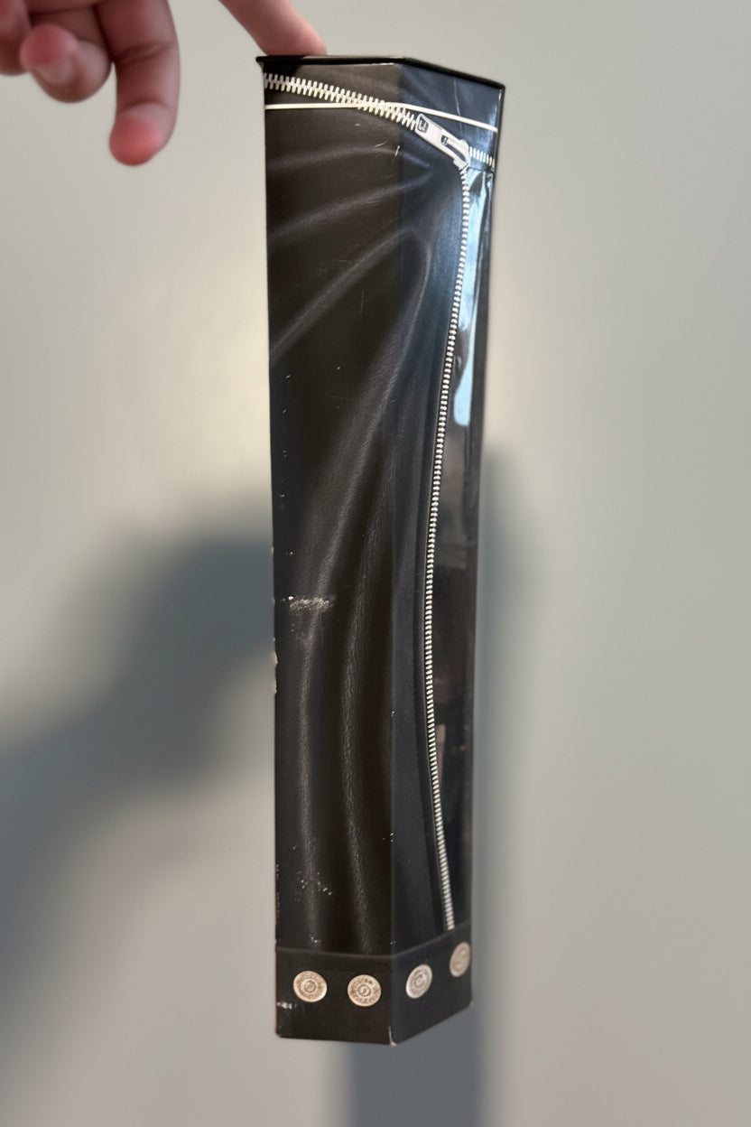 A black zipper pouch with a clear plastic side panel, held by a hand over a plaid blanket background.