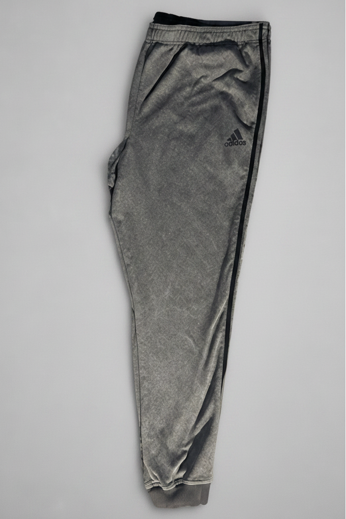 A pair of gray Adidas jogger pants laid flat on a light gray background, shown next to a yellow tape measure to indicate size.