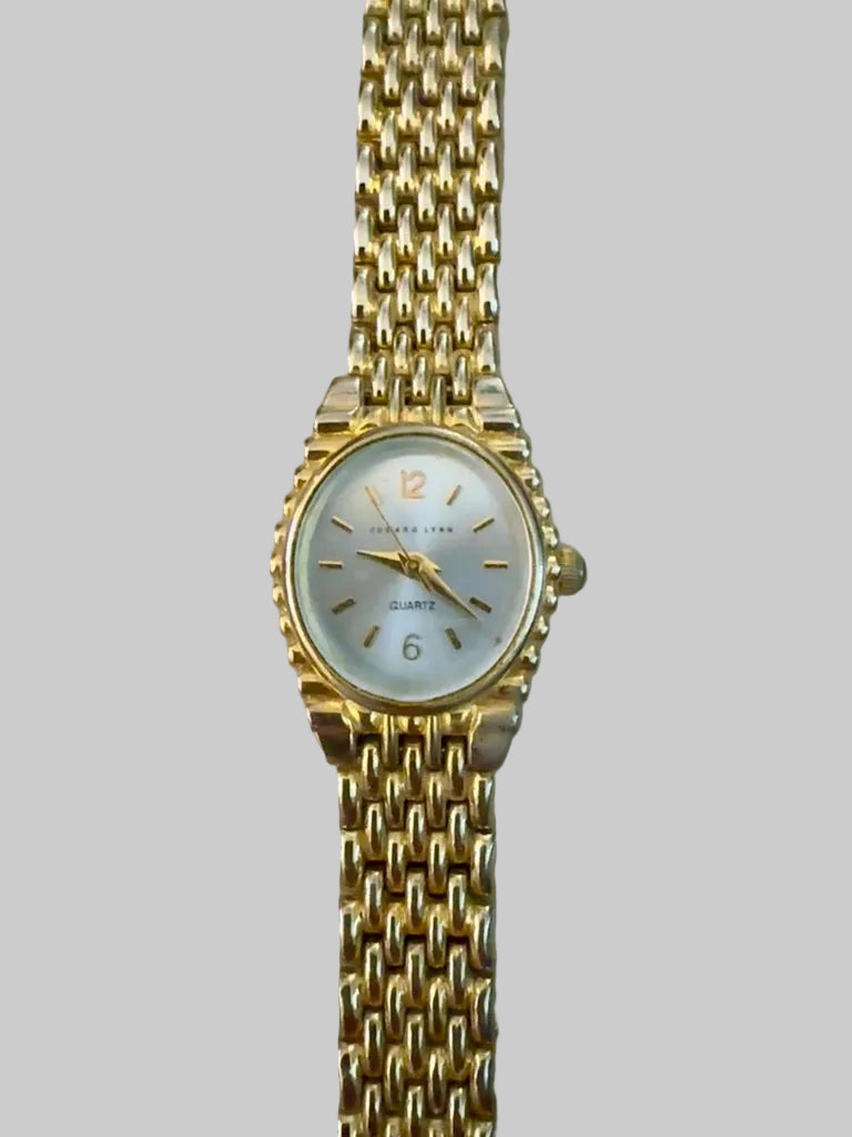 Gold wristwatch with a white face on a gray background