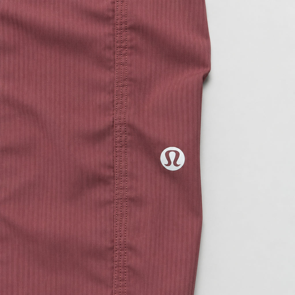 Close-up of a ribbed burgundy athletic fabric waistband with a small white circular logo featuring an 'S' on a wooden surface.