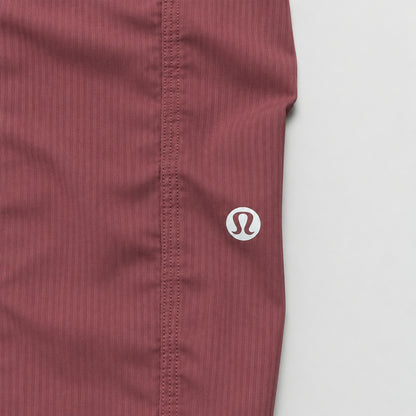 Close-up of a ribbed burgundy athletic fabric waistband with a small white circular logo featuring an 'S' on a wooden surface.