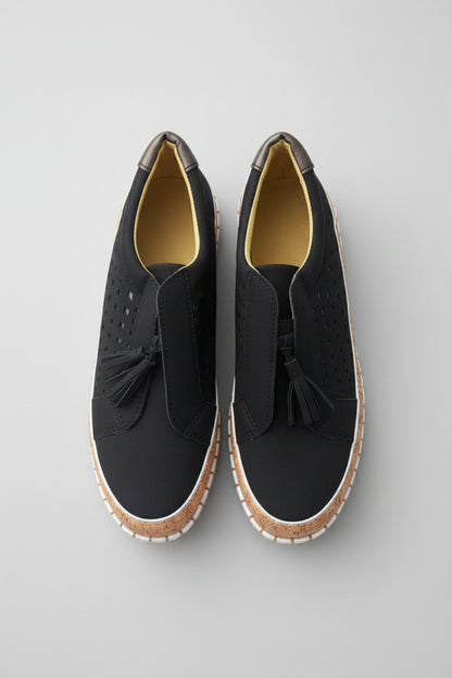 Pair of black shoes with tassels on a light wooden floor.