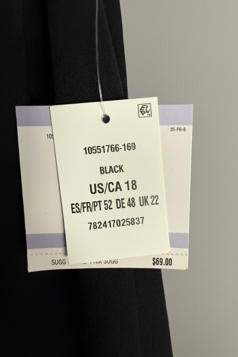 A close-up of a garment tag attached to a black fabric item, showing the text 'BLACK US/CA 18' and size information, with a textured light blue wall in the background.
