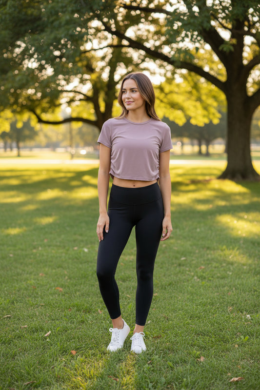 A dusty rose short-sleeve t-shirt with ruching on the right side, hanging on a white plastic hanger against a light beige wooden plank background.