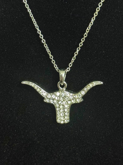 A silver-toned longhorn bull head pendant necklace paved with small clear stones, displayed on a black textured background.
