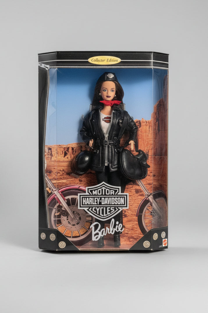 A boxed collectible Barbie doll with Harley-Davidson branding, shown in its retail packaging on a plaid fabric surface. The package features a Barbie figure in a black leather motorcycle jacket and helmet, with a desert rock scene printed behind her.