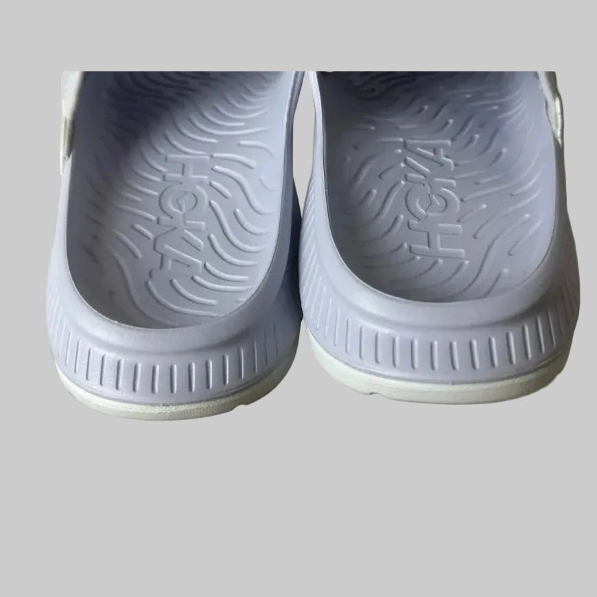 Close-up of gray shoes with 'Hoka' branding on a light gray background