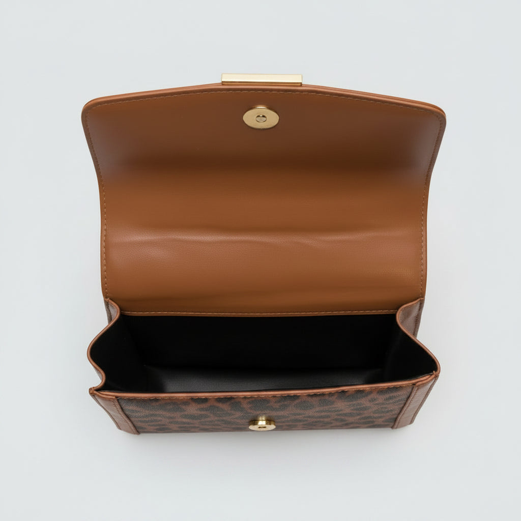 Close-up of a brown leather handbag with gold hardware on a textured surface.