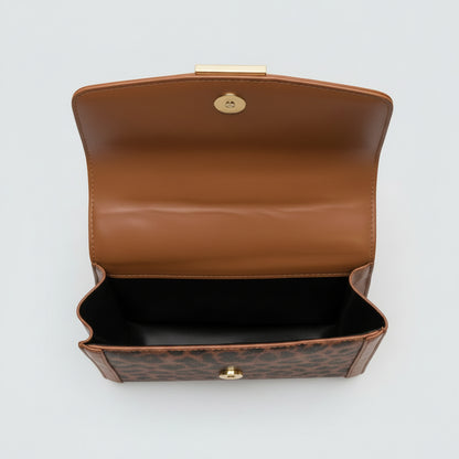Close-up of a brown leather handbag with gold hardware on a textured surface.