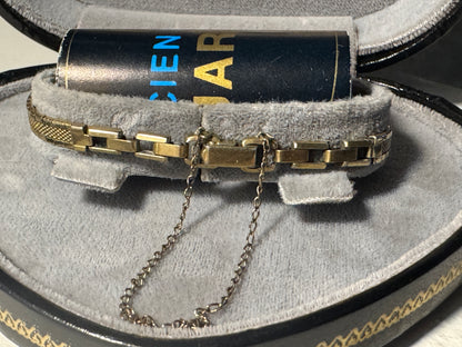 Gold bracelet with chain on gray cushion in jewelry box