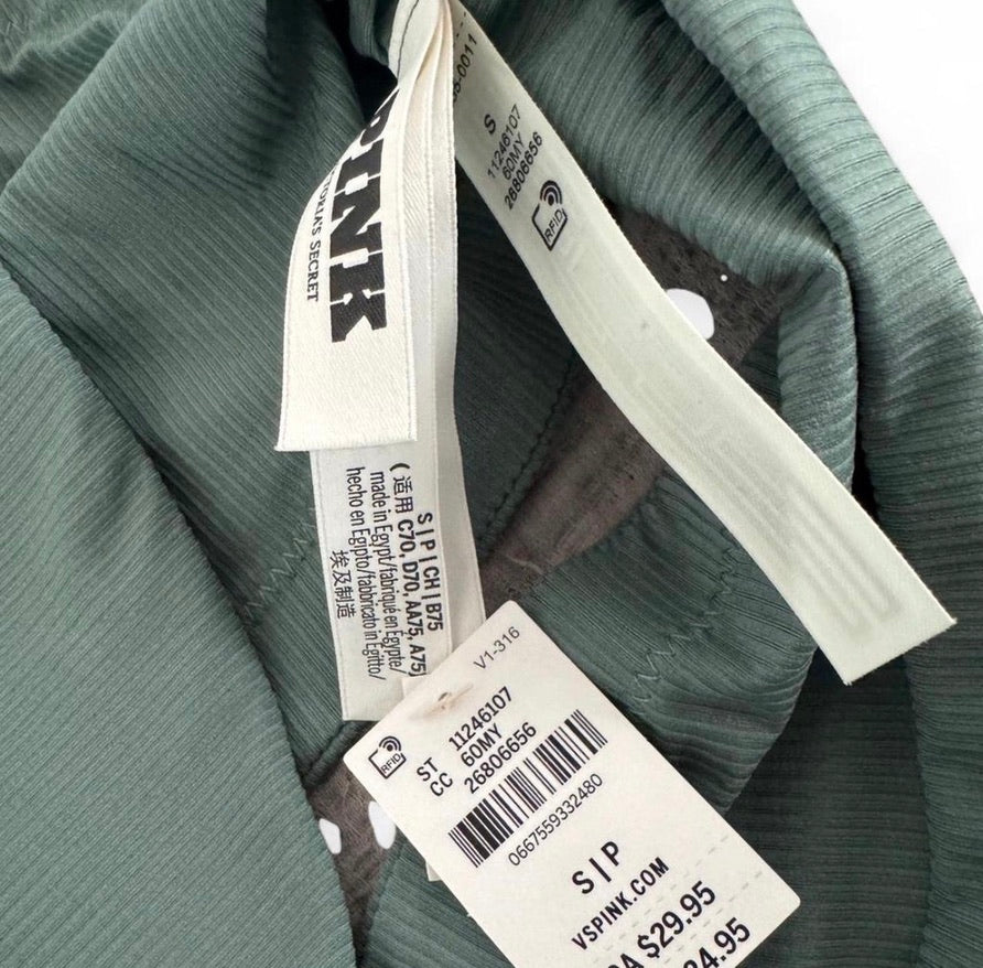 Close-up of a sage green ribbed garment showing the inner neck lining, a white sewn-in size tag, and a detachable product info tag with a barcode on a white background.