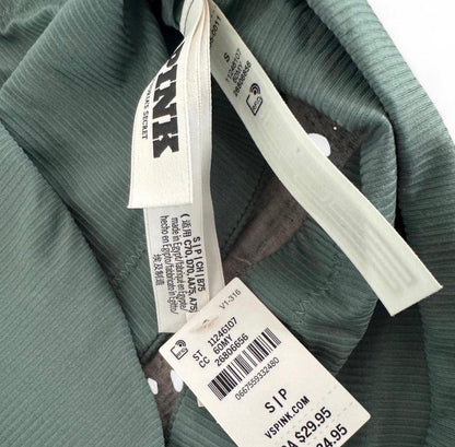 Close-up of a sage green ribbed garment showing the inner neck lining, a white sewn-in size tag, and a detachable product info tag with a barcode on a white background.