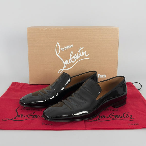 Black patent leather shoes with a branded box and pouch on a gray surface