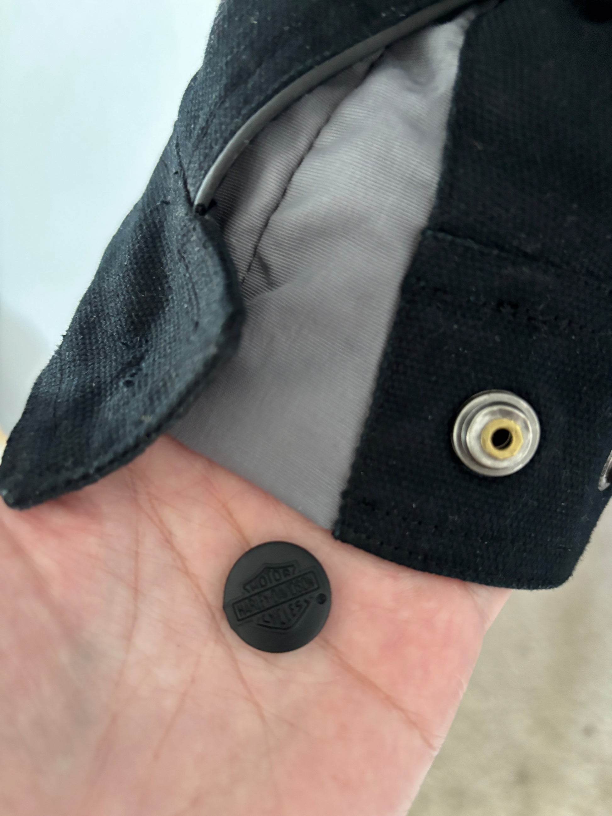 Black button held in front of a black coat with a visible brand logo.