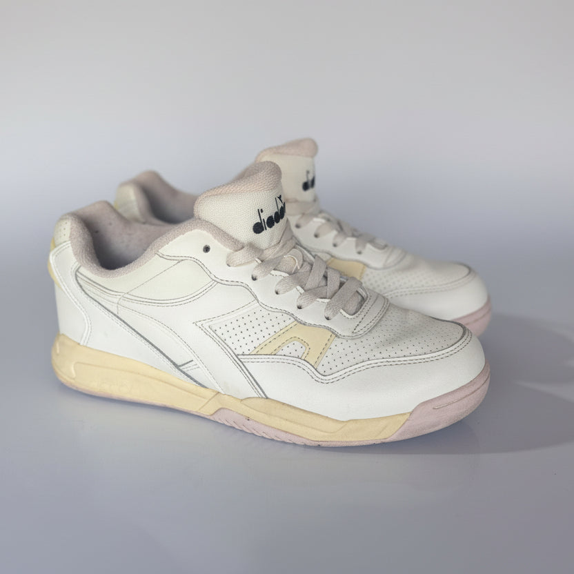 White sneakers with beige soles on a light gray surface in an indoor setting