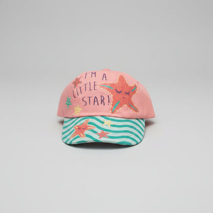 A children's baseball cap resting on a textured beige carpet. The cap features a coral pink crown with the text 'I'M A LITTLE STAR!' and embroidered orange starfish, paired with a teal and white wavy striped brim decorated with starfish and sea-creature prints.