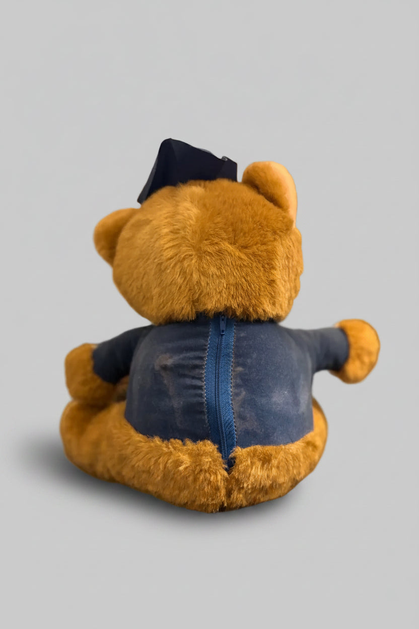 Teddy bear wearing a blue jacket on a dark surface with a blurred background