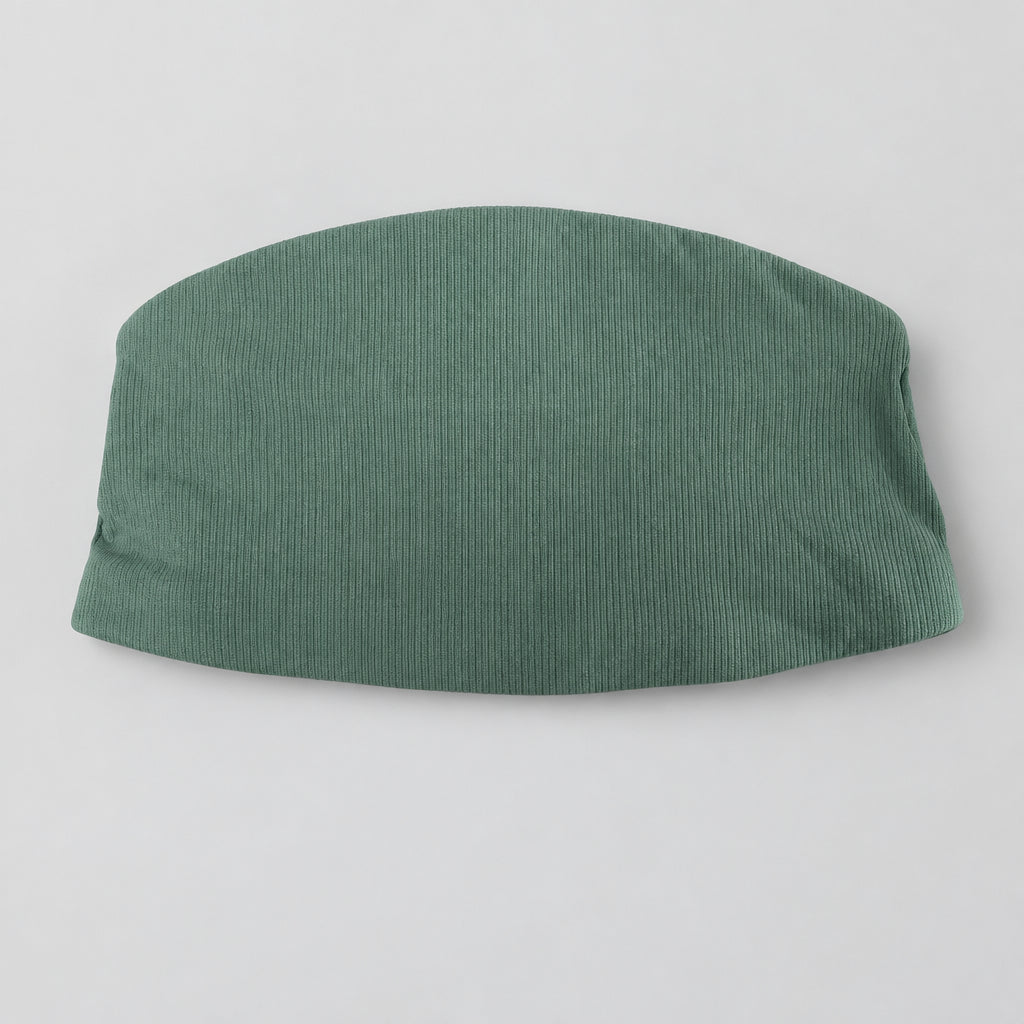 A sage green ribbed knit skirt or shorts laid flat on a textured gray blanket, with a white retail tag still attached.