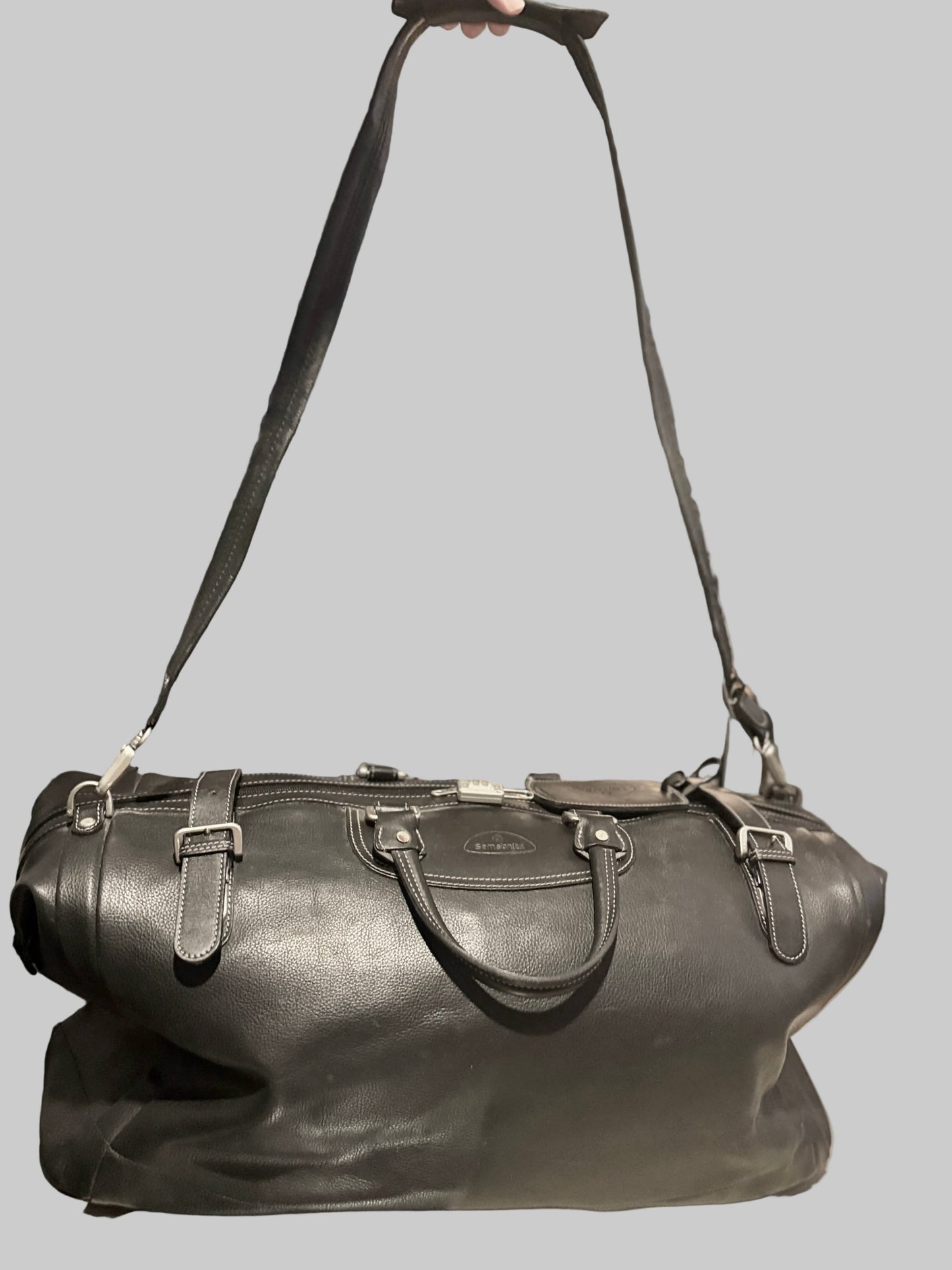 Black leather duffel bag with a strap on a gray background