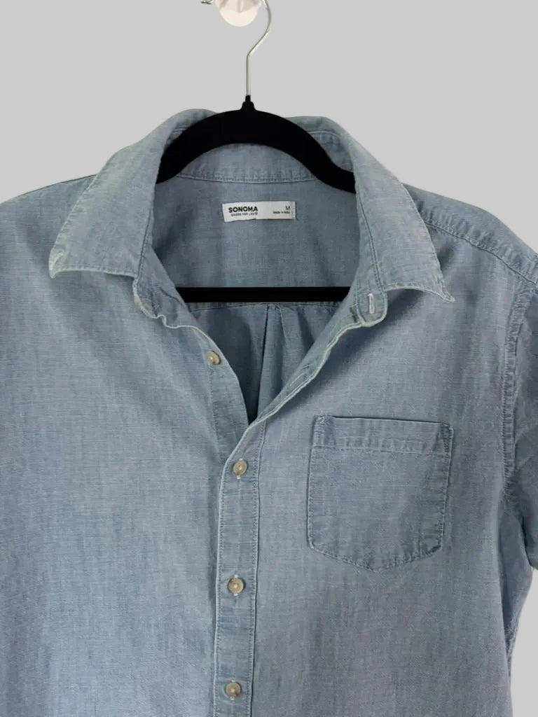 A light blue chambray button-down shirt by Domina, hanging on a black hanger against a white paneled door.