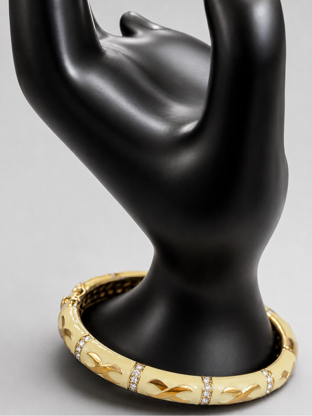 A gold hinged bangle bracelet with pavé-set clear stones and leaf-like cutouts, displayed on a black hand-shaped jewelry stand against a light gray background.