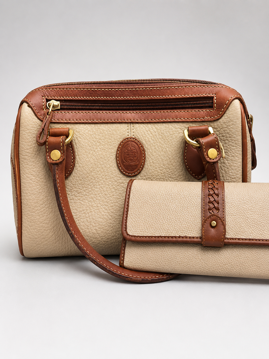 A beige pebbled leather handbag with brown leather trim and a matching zip-around wallet, photographed on a light gray studio background.