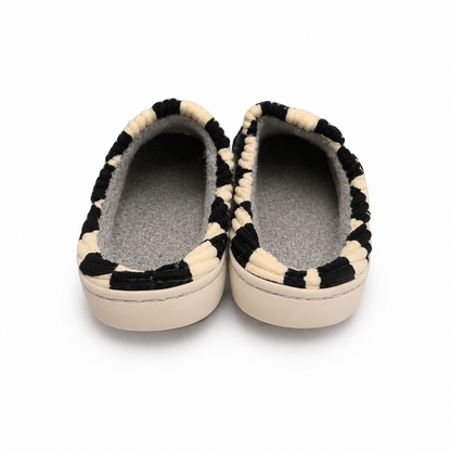 A pair of slip-on slippers with a black and cream striped textured fabric upper and a soft gray fleece lining, shown from a top-down view on a white background.
