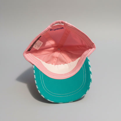 A two-tone baseball cap with a pink crown and a teal-green curved brim, photographed from above on a gray textured blanket. The brand 'BONSAI' is visible on the inner crown.