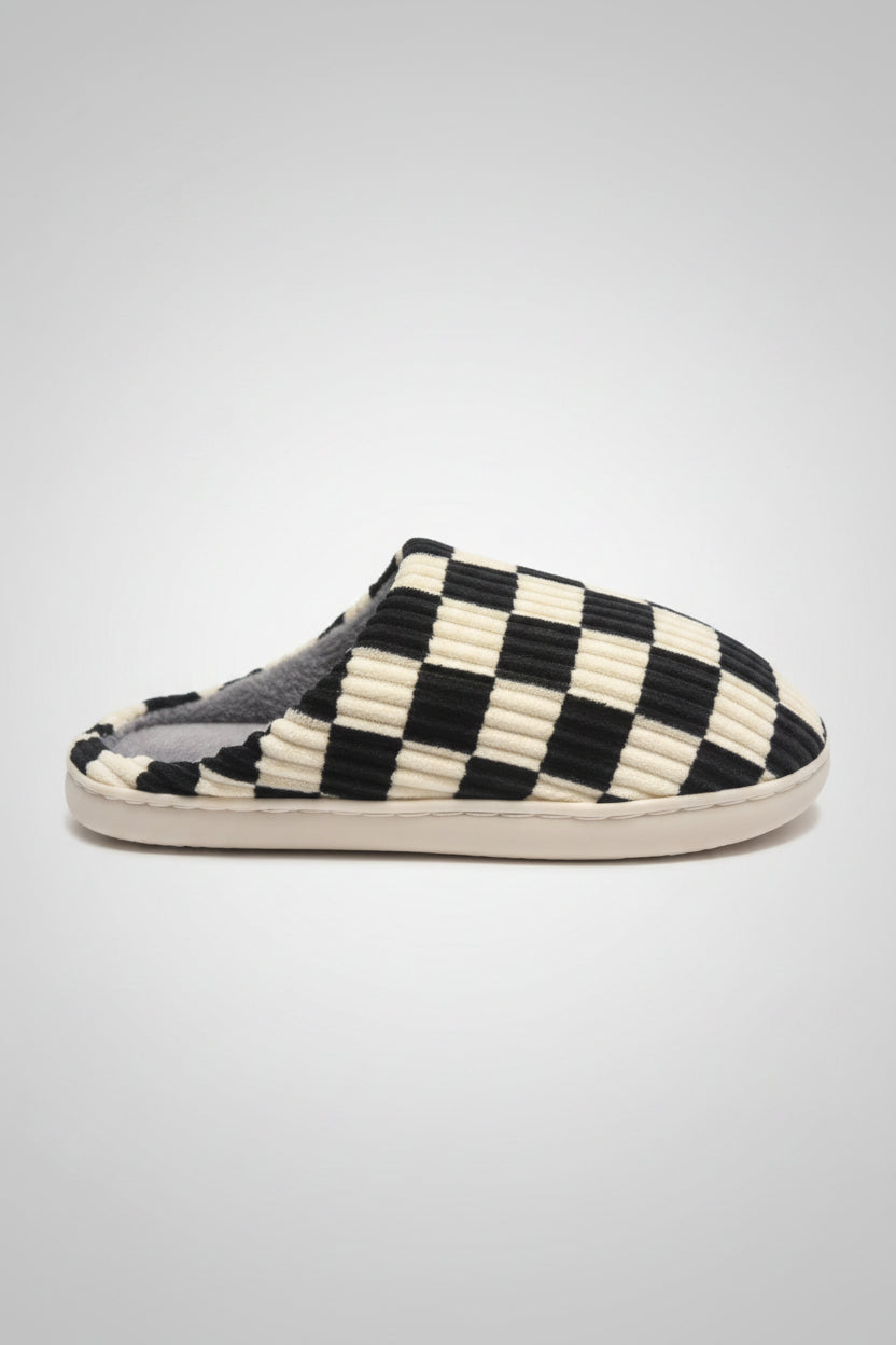 A single slip-on mule slipper with a black and cream checkerboard patterned upper, shown on a textured gray surface.