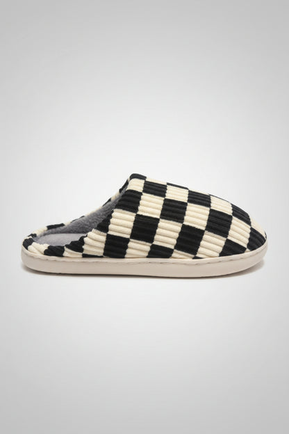 A single slip-on mule slipper with a black and cream checkerboard patterned upper, shown on a textured gray surface.