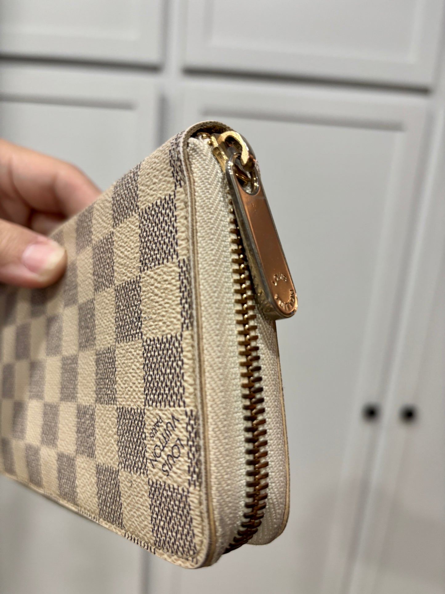 Louis Vuitton wallet with checkered pattern held by a hand against a neutral background