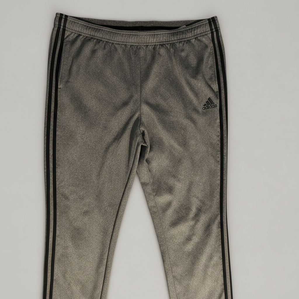 A pair of gray Adidas track pants with black side stripes, shown with a yellow measuring tape across the waistband to indicate size, on a light gray background.