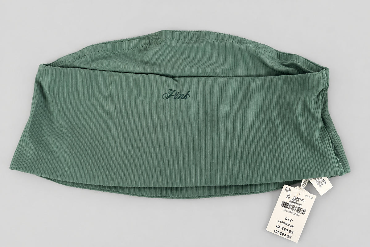 A folded sage green ribbed knit garment, likely leggings or a pant leg, with a small dark script logo on the side and a white retail tag attached, laid flat on a textured gray fabric background.
