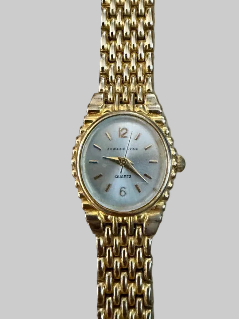 Gold wristwatch with a chain strap on a beige background