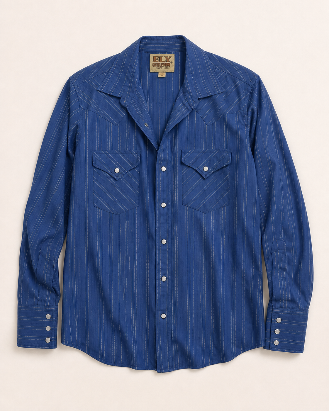 A blue long-sleeve western shirt with thin white vertical pinstripes, featuring two buttoned chest pockets and a pointed collar, laid flat against a light beige background.