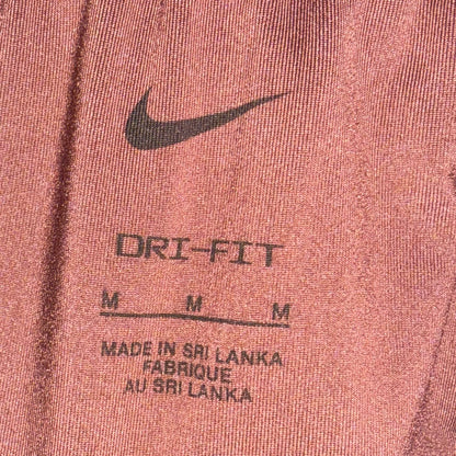 Close-up of a Nike garment, likely sweatpants or shorts, showing the elastic waistband, a black Nike swoosh, and printed text reading 'ORI-FIT' with size markings and 'Made in Sri Lanka' on a heathered dusty rose fabric.