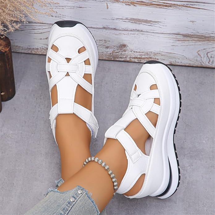 White sandals with black soles worn by a person on a gray surface.