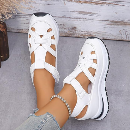 White sandals with black soles worn by a person on a gray surface.